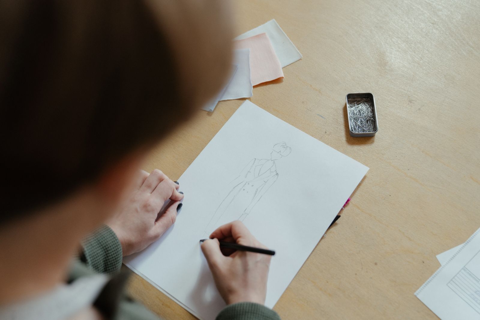 Designer sketching a coat beside fabric swatches and pins, showing the types of intellectual property in fashion