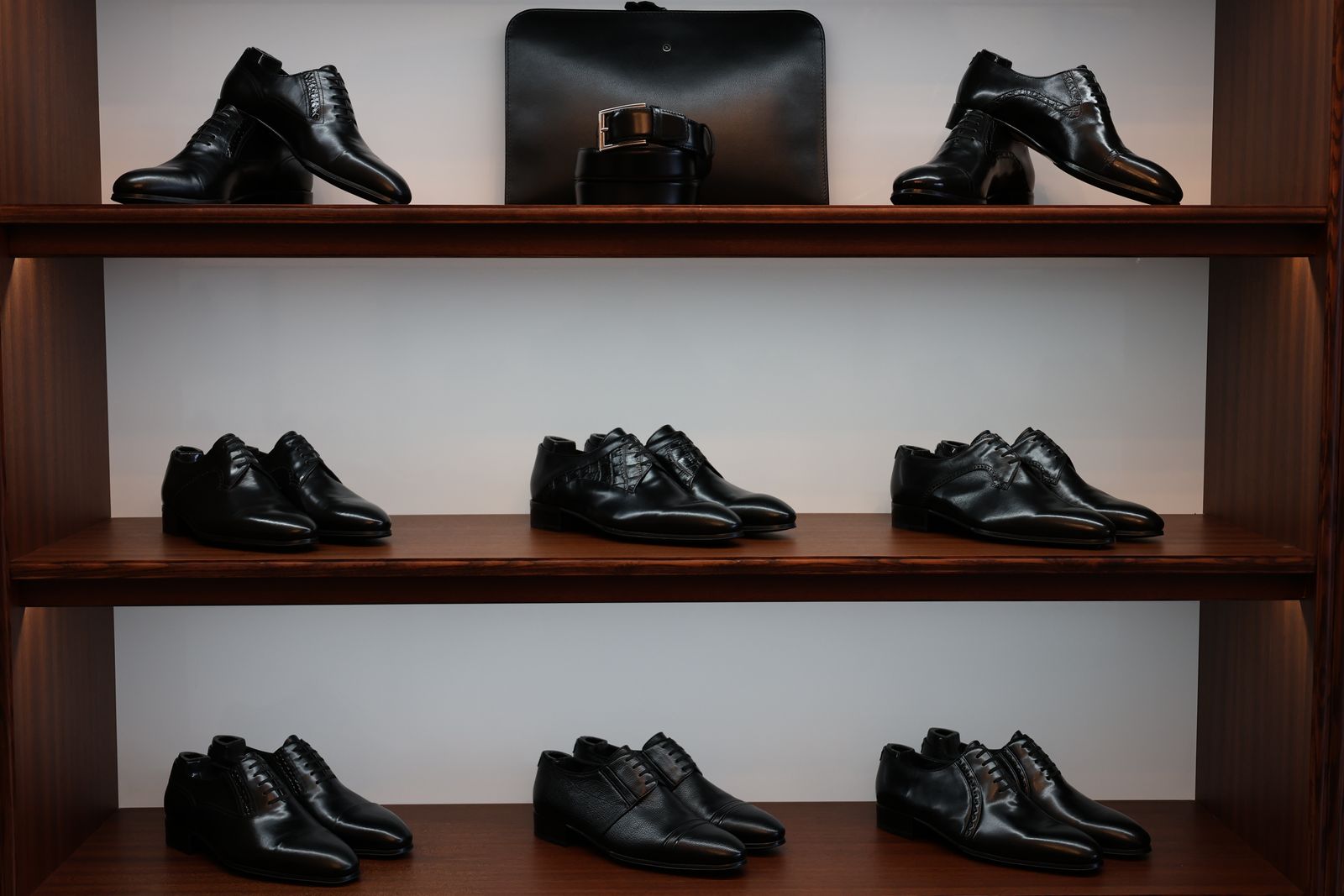 Black dress shoes, a belt and a document case displayed on three wooden shelves in a store